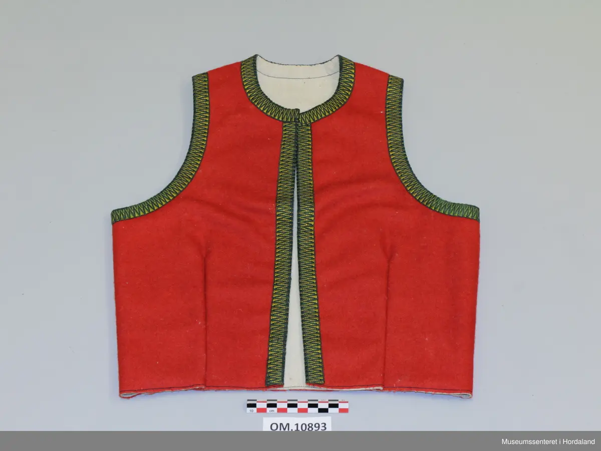 Raudt bunadsliv i ull, med grøn og gul krokakvarding i silke rundt armhola, hals og i front. Ikkje på skuldrar. Fora. Eitt innsnitt på kvart forstykke. Fire hekter til attlat framme.