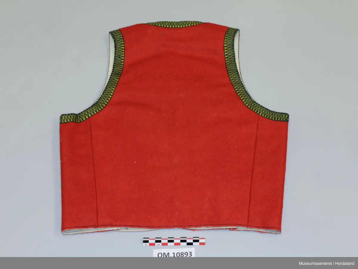 Raudt bunadsliv i ull, med grøn og gul krokakvarding i silke rundt armhola, hals og i front. Ikkje på skuldrar. Fora. Eitt innsnitt på kvart forstykke. Fire hekter til attlat framme.