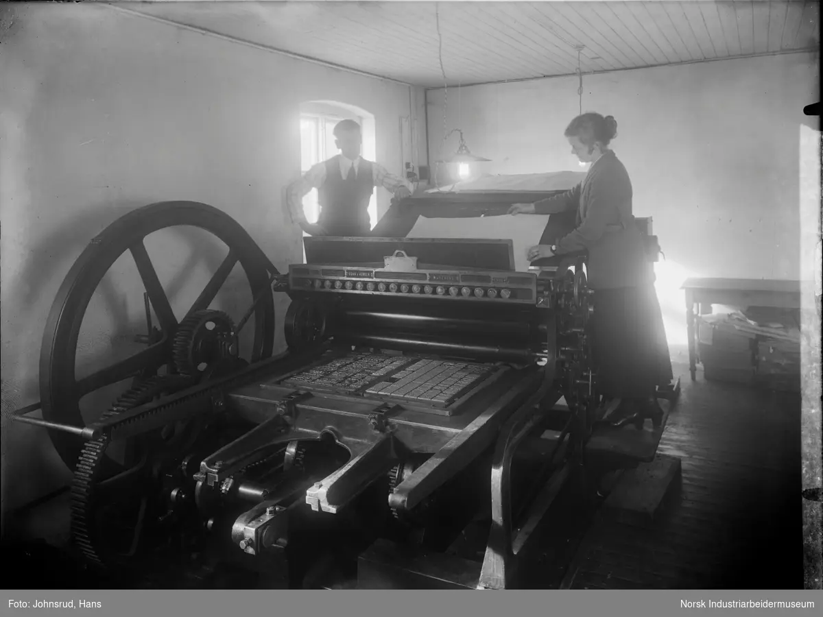 En kvinne og en mann som jobber ved en trykkpresse. Bilde fra Telemarkspostens lokaler.