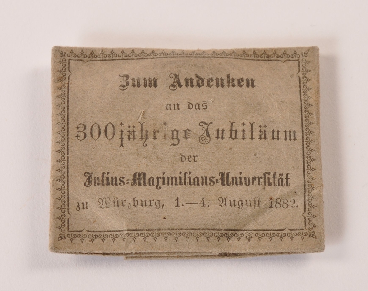 Sirkulær minnemedalje i metall, muligens sølv. Til minne om 300-års dagen av Julius Maximilians universtet i Würzburg. adversen: Portrett Ludvig av Bayern. Reversen: Våpenskjold med tekst. Ligger i brettet papirark med påtrykket forklaring av jubileet.