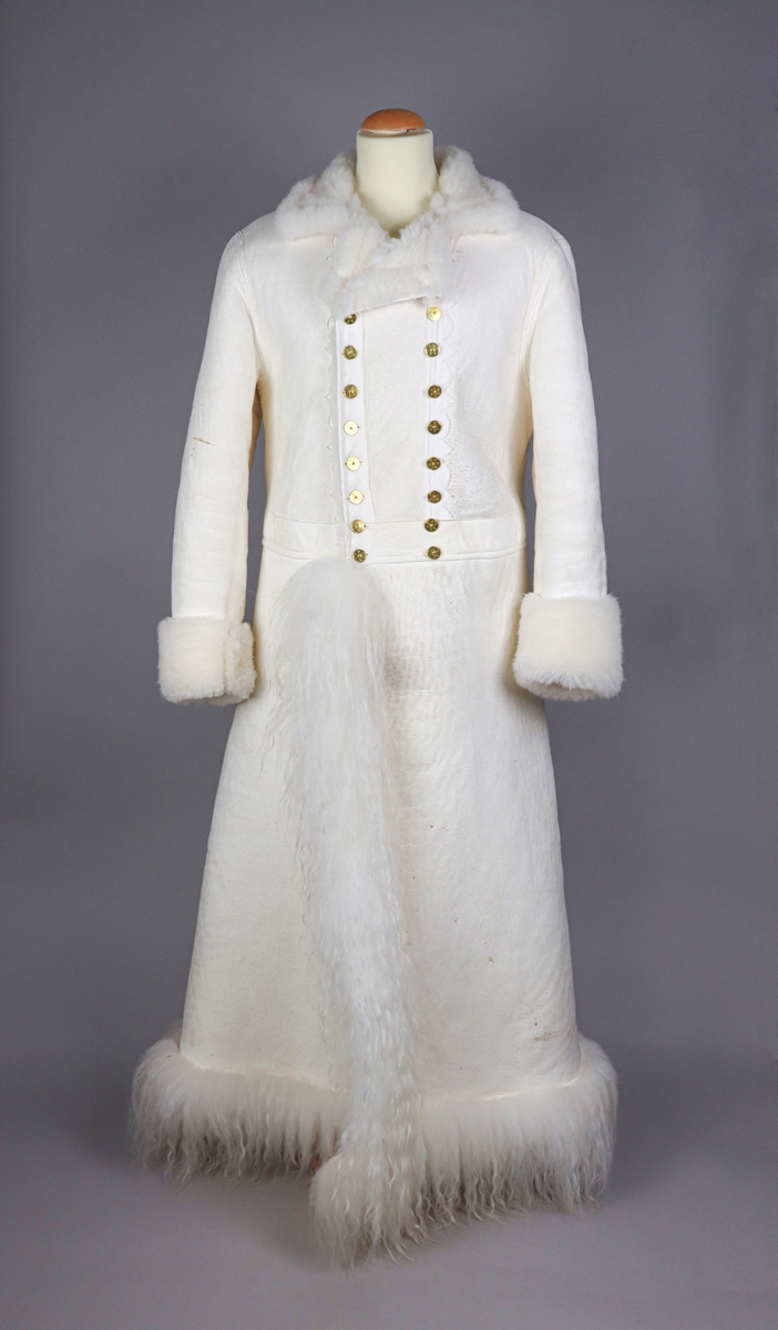 Hellång vit fårskinnspäls till mansdräkter från Västerdalarna. Pälssidan vänd innåt. Dubbelknäppning med 9 par mässingsknappar med sexuddiga stjärnorn på. Pälsen har långa pälslocksbräm längs neder- och framkanten, samt kortklippta uppvikta bräm vid ärmsluten.