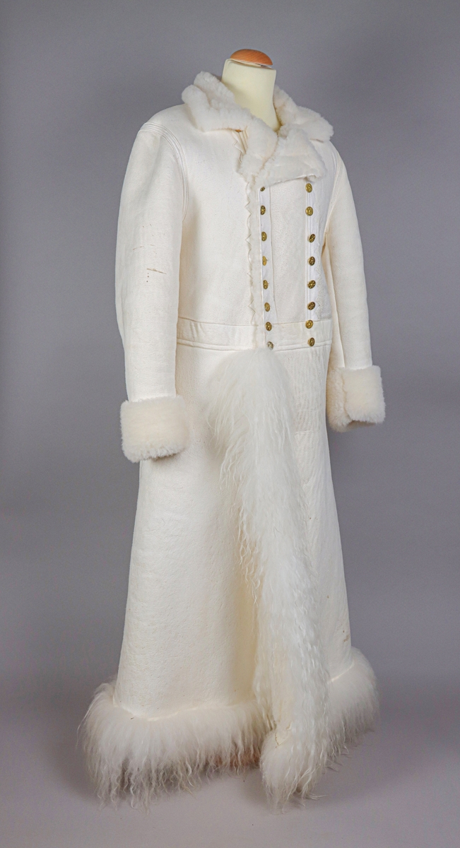 Hellång vit fårskinnspäls till mansdräkter från Västerdalarna. Pälssidan vänd innåt. Dubbelknäppning med 9 par mässingsknappar med sexuddiga stjärnorn på. Pälsen har långa pälslocksbräm längs neder- och framkanten, samt kortklippta uppvikta bräm vid ärmsluten.