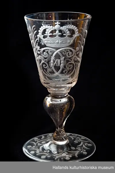 Pokal av glas med Karl XII:s krönta monogram i bladcartouche. Fot med graverad växtranka. Droppformig ihålig midja. Böhmisk typ.