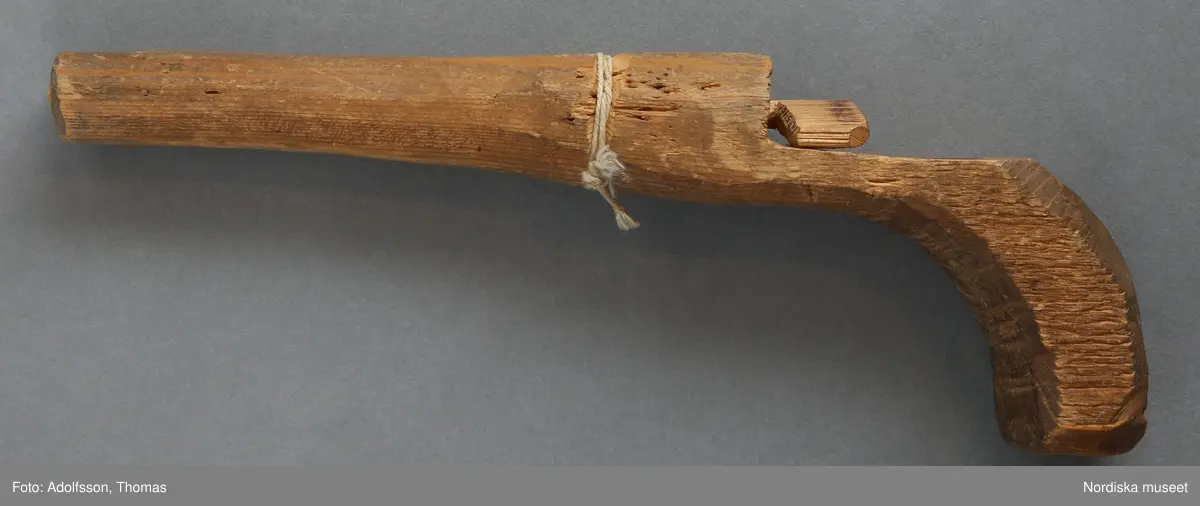 Inventering Sesam 1996-1999:
L 20,B 2,7 cm
Ärtpistol av trä i både pipa och stock. "Påskjutare" att föra in i röret,  tillverkad senare.
Ett vitt bomullssnöre runt pipan liggande i en skåra.
Helena Carlsson 1996