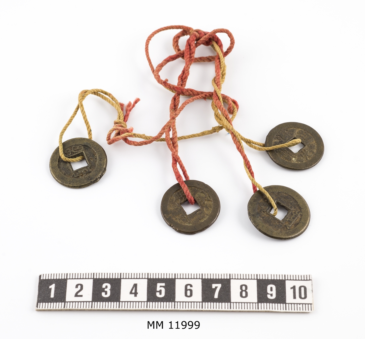 Fyra kinesiska spelmarker av metall. Runda med i mitten ett fyrkantigt hål. Försedda med skrivtecken.