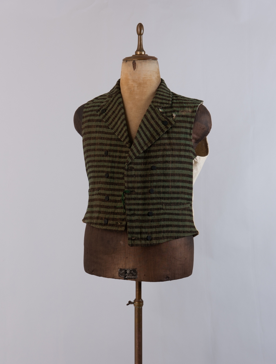 Dobbeltspent vest i ullverken, stripet i grønt og svart (sauesvart) med brun renning. Dobbel rygg i bomullslerret. Halvlinslerret (bomull/stry) i fôret i framstykkene. Vesten har fire knapphull sydd med kamgarnsullgarn og svarte knapper trukket med svart bomullssateng med brun renning. Plagget har nedbrettet krage og slag/reverser som kan kneppes mot bolen. Knapp og knapphull. Vesten buer ned midt framme og har svakt skråstilte lommer. Vattering av stry i framstykkene. I ryggen buer vesten opp midt bak. Den er vrangsydd langs ytterkantene og stukket ned med maskin, 0,8 cm fra kanten. (Registrering ved Bunad- og folkedraktrådet/Norsk institutt for bunad og folkedrakt v/Jon Fredrik Skauge, 2005, revidert v/Bjørn Sverre Hol Haugen, 2020.)