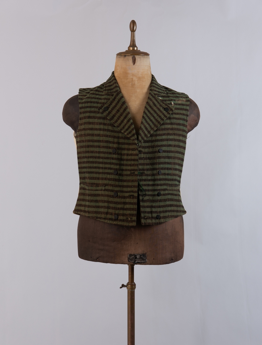 Dobbeltspent vest i ullverken, stripet i grønt og svart (sauesvart) med brun renning. Dobbel rygg i bomullslerret. Halvlinslerret (bomull/stry) i fôret i framstykkene. Vesten har fire knapphull sydd med kamgarnsullgarn og svarte knapper trukket med svart bomullssateng med brun renning. Plagget har nedbrettet krage og slag/reverser som kan kneppes mot bolen. Knapp og knapphull. Vesten buer ned midt framme og har svakt skråstilte lommer. Vattering av stry i framstykkene. I ryggen buer vesten opp midt bak. Den er vrangsydd langs ytterkantene og stukket ned med maskin, 0,8 cm fra kanten. (Registrering ved Bunad- og folkedraktrådet/Norsk institutt for bunad og folkedrakt v/Jon Fredrik Skauge, 2005, revidert v/Bjørn Sverre Hol Haugen, 2020.)