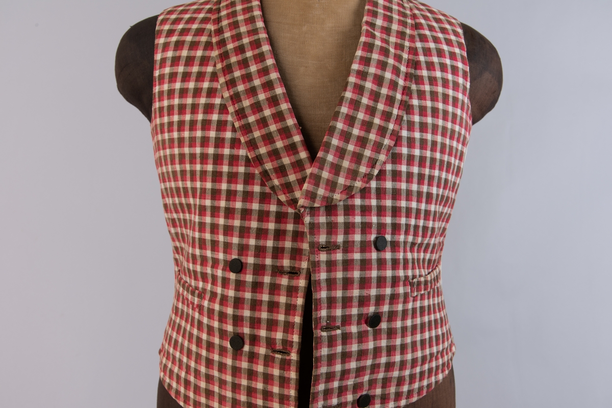 Vest i rutet bomullslerret i fargene rødt, olivengrønt/grønnnbrunt og ubleiket hvitt. Fôr og rygg i linlerret. Vesten er dobbeltspent med svarte, stofftrukne knapper. Den har sjalskrage og spensel i ryggen. Plagget er helt håndsydd. På forstykkene er det to lett skråstilte lommer og vesten buer ned midt foran.