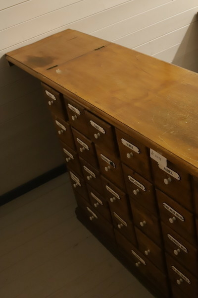 Lita skuff i treverk med lakka front. Høyrer til i apotekdisken. Fronten har kvit porselensknott og kvitt skilt med medisinnamn i svart skrift: CORT.FRUCT.AUR