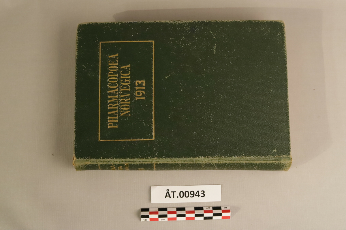 Mørkegrøn bok med gulldetaljer: Den norske farmakopø 1913 (Pharmacopoea Norvegica ed.IV.). Utgit paa offentlig foranstaltning. Kristiania, forlagt av H.Aschehoug & Vo (W.Nygaard) 1913.