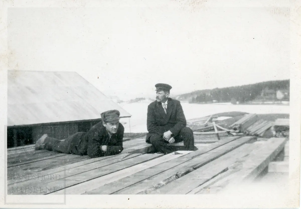 To menn sitter og ligger på plankestabel på Sagatangen