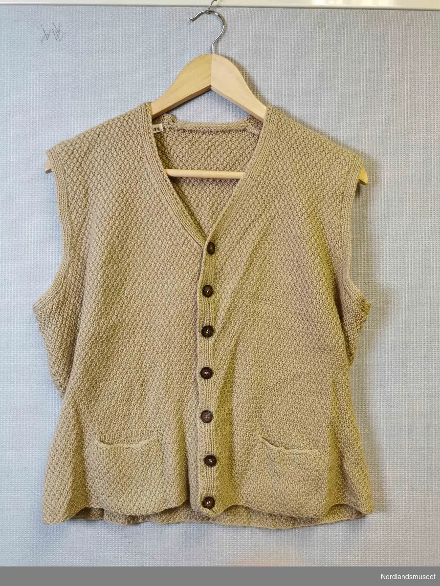 Beige strikket vest til dame. Perlestrikk. Påsydd belte bak. To lommer i front. Brune knapper.