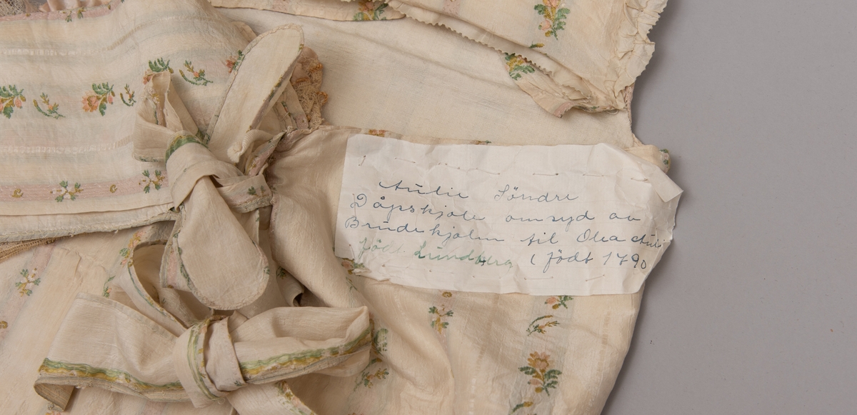 Dåpsløyert med pute samt løse ermer og en blondekrage. Løyerten er sydd av et ecrufarget silkestoff med stripemønster hvor det er innvevd blomster og blader. Løyerten lukkes med to sett knyteband, det ene settet er enkle bendelband som også snøres gjennom løpeganger, mens det andre er silkeband sydd av stoffet. Langs nederkant har løyerten en rynket kant av hovedstoffet samt et rynket dekorband av ensfarget, ecrufarget silke. Løyerten er fôret med linlerret. Ermene er sydd av hovedstoffet og har dekor av samme rynkede silkeband, men er uten fôr. Trolig har ermene vært tråklet til ei undertrøye som dåpsbarnet har hatt under reiven. Kragen, som er av tyllblonde, trolig i lin med silketråder og silkeband, er vid, så den har trolig vært rynket med ei snor og tråklet til undertrøya. Da barnet lå som en reivet bylt inne i løyerten, var det bare ermene som kom til syne, derfor var det ikke nødvendig med ei hel trøye. Alternativt kan det være at ermene tidligere har sittet på ei silketrøye som nå er fjernet.