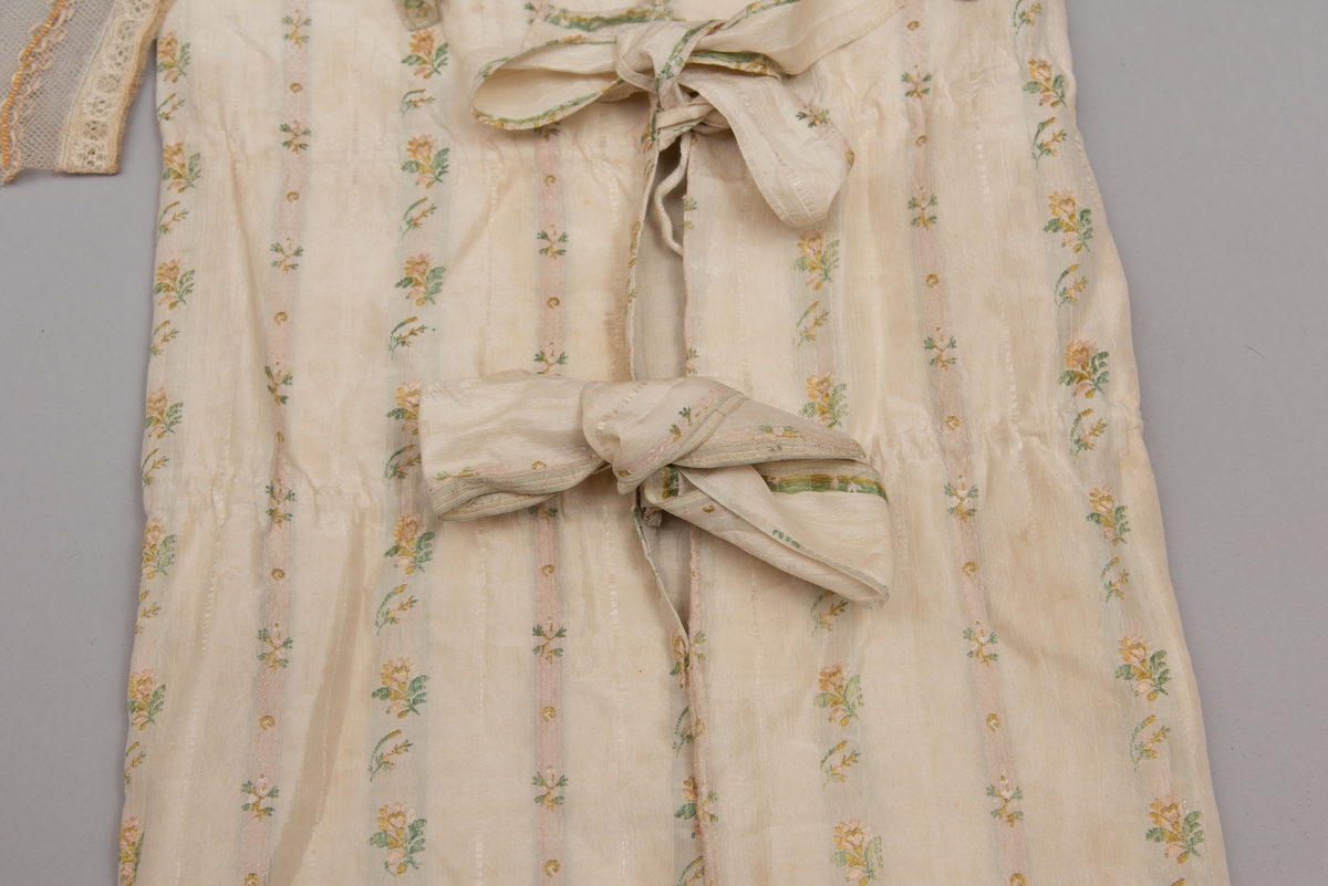 Dåpsløyert med pute samt løse ermer og en blondekrage. Løyerten er sydd av et ecrufarget silkestoff med stripemønster hvor det er innvevd blomster og blader. Løyerten lukkes med to sett knyteband, det ene settet er enkle bendelband som også snøres gjennom løpeganger, mens det andre er silkeband sydd av stoffet. Langs nederkant har løyerten en rynket kant av hovedstoffet samt et rynket dekorband av ensfarget, ecrufarget silke. Løyerten er fôret med linlerret. Ermene er sydd av hovedstoffet og har dekor av samme rynkede silkeband, men er uten fôr. Trolig har ermene vært tråklet til ei undertrøye som dåpsbarnet har hatt under reiven. Kragen, som er av tyllblonde, trolig i lin med silketråder og silkeband, er vid, så den har trolig vært rynket med ei snor og tråklet til undertrøya. Da barnet lå som en reivet bylt inne i løyerten, var det bare ermene som kom til syne, derfor var det ikke nødvendig med ei hel trøye. Alternativt kan det være at ermene tidligere har sittet på ei silketrøye som nå er fjernet.