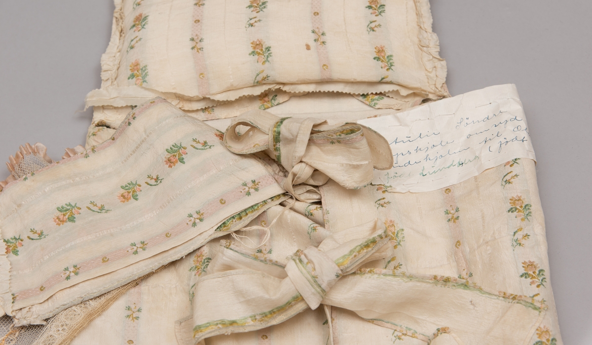 Dåpsløyert med pute samt løse ermer og en blondekrage. Løyerten er sydd av et ecrufarget silkestoff med stripemønster hvor det er innvevd blomster og blader. Løyerten lukkes med to sett knyteband, det ene settet er enkle bendelband som også snøres gjennom løpeganger, mens det andre er silkeband sydd av stoffet. Langs nederkant har løyerten en rynket kant av hovedstoffet samt et rynket dekorband av ensfarget, ecrufarget silke. Løyerten er fôret med linlerret. Ermene er sydd av hovedstoffet og har dekor av samme rynkede silkeband, men er uten fôr. Trolig har ermene vært tråklet til ei undertrøye som dåpsbarnet har hatt under reiven. Kragen, som er av tyllblonde, trolig i lin med silketråder og silkeband, er vid, så den har trolig vært rynket med ei snor og tråklet til undertrøya. Da barnet lå som en reivet bylt inne i løyerten, var det bare ermene som kom til syne, derfor var det ikke nødvendig med ei hel trøye. Alternativt kan det være at ermene tidligere har sittet på ei silketrøye som nå er fjernet.