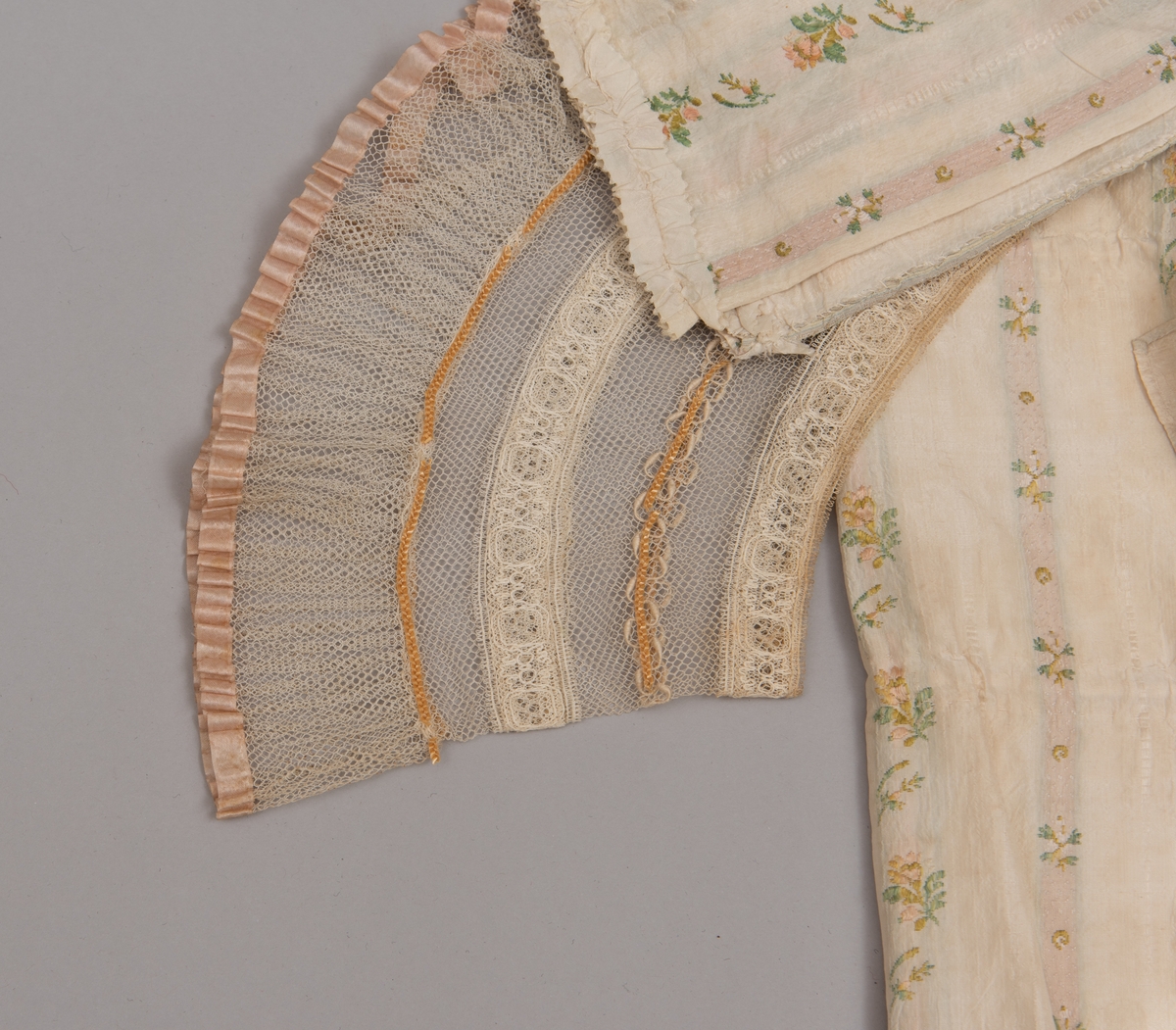 Dåpsløyert med pute samt løse ermer og en blondekrage. Løyerten er sydd av et ecrufarget silkestoff med stripemønster hvor det er innvevd blomster og blader. Løyerten lukkes med to sett knyteband, det ene settet er enkle bendelband som også snøres gjennom løpeganger, mens det andre er silkeband sydd av stoffet. Langs nederkant har løyerten en rynket kant av hovedstoffet samt et rynket dekorband av ensfarget, ecrufarget silke. Løyerten er fôret med linlerret. Ermene er sydd av hovedstoffet og har dekor av samme rynkede silkeband, men er uten fôr. Trolig har ermene vært tråklet til ei undertrøye som dåpsbarnet har hatt under reiven. Kragen, som er av tyllblonde, trolig i lin med silketråder og silkeband, er vid, så den har trolig vært rynket med ei snor og tråklet til undertrøya. Da barnet lå som en reivet bylt inne i løyerten, var det bare ermene som kom til syne, derfor var det ikke nødvendig med ei hel trøye. Alternativt kan det være at ermene tidligere har sittet på ei silketrøye som nå er fjernet.