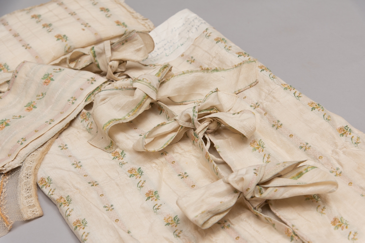 Dåpsløyert med pute samt løse ermer og en blondekrage. Løyerten er sydd av et ecrufarget silkestoff med stripemønster hvor det er innvevd blomster og blader. Løyerten lukkes med to sett knyteband, det ene settet er enkle bendelband som også snøres gjennom løpeganger, mens det andre er silkeband sydd av stoffet. Langs nederkant har løyerten en rynket kant av hovedstoffet samt et rynket dekorband av ensfarget, ecrufarget silke. Løyerten er fôret med linlerret. Ermene er sydd av hovedstoffet og har dekor av samme rynkede silkeband, men er uten fôr. Trolig har ermene vært tråklet til ei undertrøye som dåpsbarnet har hatt under reiven. Kragen, som er av tyllblonde, trolig i lin med silketråder og silkeband, er vid, så den har trolig vært rynket med ei snor og tråklet til undertrøya. Da barnet lå som en reivet bylt inne i løyerten, var det bare ermene som kom til syne, derfor var det ikke nødvendig med ei hel trøye. Alternativt kan det være at ermene tidligere har sittet på ei silketrøye som nå er fjernet.