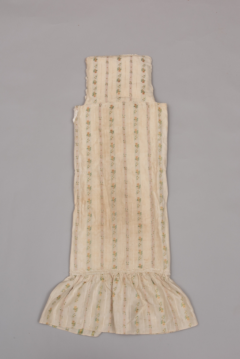 Dåpsløyert med pute samt løse ermer og en blondekrage. Løyerten er sydd av et ecrufarget silkestoff med stripemønster hvor det er innvevd blomster og blader. Løyerten lukkes med to sett knyteband, det ene settet er enkle bendelband som også snøres gjennom løpeganger, mens det andre er silkeband sydd av stoffet. Langs nederkant har løyerten en rynket kant av hovedstoffet samt et rynket dekorband av ensfarget, ecrufarget silke. Løyerten er fôret med linlerret. Ermene er sydd av hovedstoffet og har dekor av samme rynkede silkeband, men er uten fôr. Trolig har ermene vært tråklet til ei undertrøye som dåpsbarnet har hatt under reiven. Kragen, som er av tyllblonde, trolig i lin med silketråder og silkeband, er vid, så den har trolig vært rynket med ei snor og tråklet til undertrøya. Da barnet lå som en reivet bylt inne i løyerten, var det bare ermene som kom til syne, derfor var det ikke nødvendig med ei hel trøye. Alternativt kan det være at ermene tidligere har sittet på ei silketrøye som nå er fjernet.