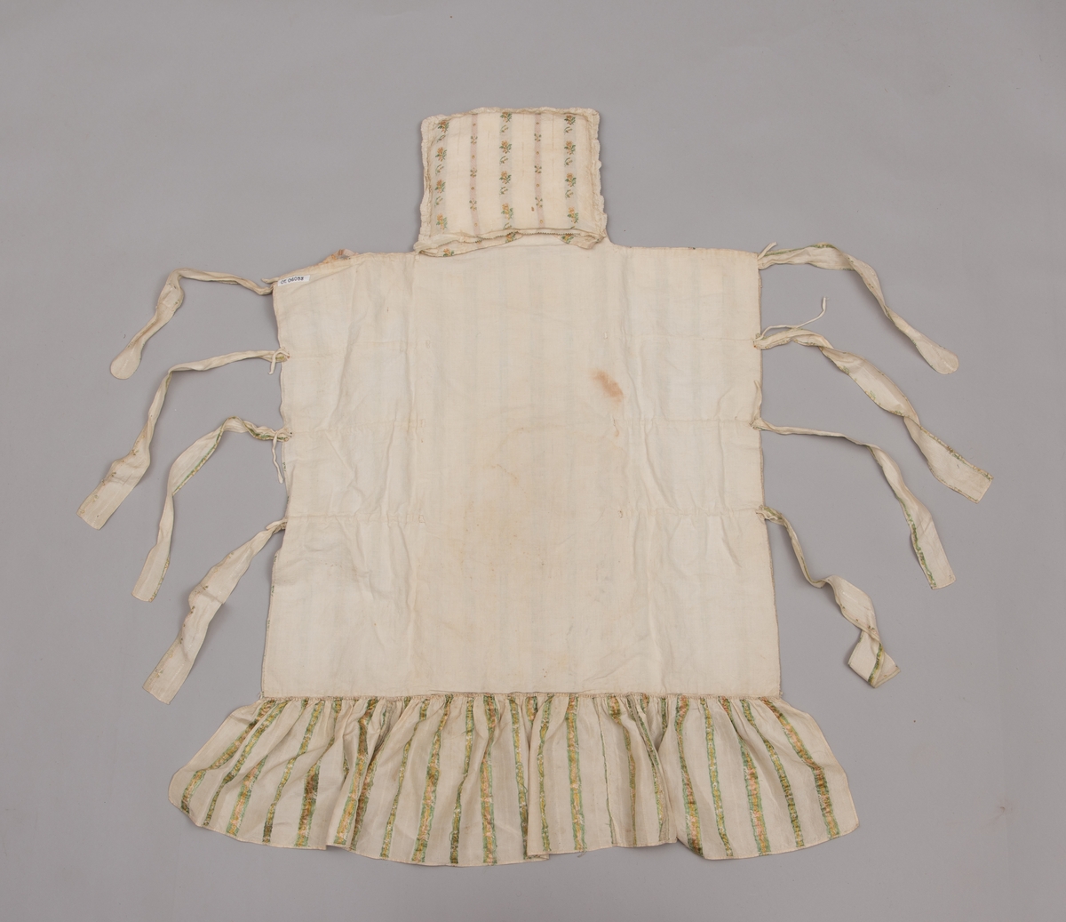 Dåpsløyert med pute samt løse ermer og en blondekrage. Løyerten er sydd av et ecrufarget silkestoff med stripemønster hvor det er innvevd blomster og blader. Løyerten lukkes med to sett knyteband, det ene settet er enkle bendelband som også snøres gjennom løpeganger, mens det andre er silkeband sydd av stoffet. Langs nederkant har løyerten en rynket kant av hovedstoffet samt et rynket dekorband av ensfarget, ecrufarget silke. Løyerten er fôret med linlerret. Ermene er sydd av hovedstoffet og har dekor av samme rynkede silkeband, men er uten fôr. Trolig har ermene vært tråklet til ei undertrøye som dåpsbarnet har hatt under reiven. Kragen, som er av tyllblonde, trolig i lin med silketråder og silkeband, er vid, så den har trolig vært rynket med ei snor og tråklet til undertrøya. Da barnet lå som en reivet bylt inne i løyerten, var det bare ermene som kom til syne, derfor var det ikke nødvendig med ei hel trøye. Alternativt kan det være at ermene tidligere har sittet på ei silketrøye som nå er fjernet.