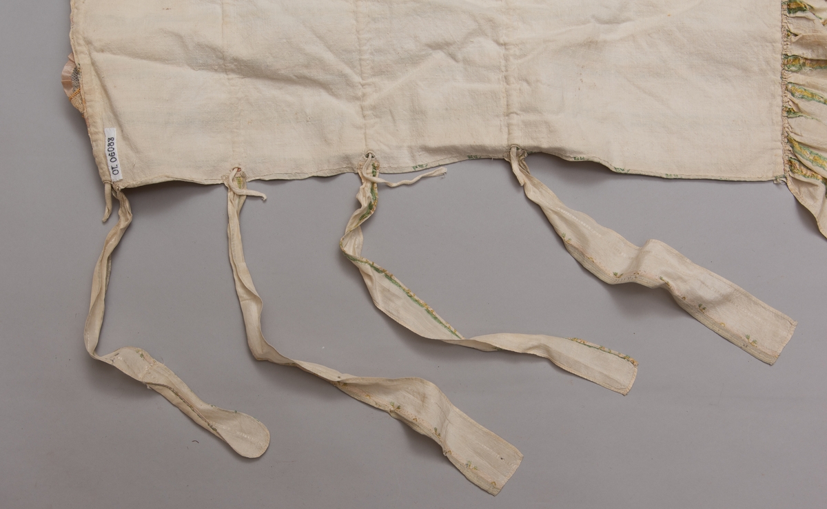 Dåpsløyert med pute samt løse ermer og en blondekrage. Løyerten er sydd av et ecrufarget silkestoff med stripemønster hvor det er innvevd blomster og blader. Løyerten lukkes med to sett knyteband, det ene settet er enkle bendelband som også snøres gjennom løpeganger, mens det andre er silkeband sydd av stoffet. Langs nederkant har løyerten en rynket kant av hovedstoffet samt et rynket dekorband av ensfarget, ecrufarget silke. Løyerten er fôret med linlerret. Ermene er sydd av hovedstoffet og har dekor av samme rynkede silkeband, men er uten fôr. Trolig har ermene vært tråklet til ei undertrøye som dåpsbarnet har hatt under reiven. Kragen, som er av tyllblonde, trolig i lin med silketråder og silkeband, er vid, så den har trolig vært rynket med ei snor og tråklet til undertrøya. Da barnet lå som en reivet bylt inne i løyerten, var det bare ermene som kom til syne, derfor var det ikke nødvendig med ei hel trøye. Alternativt kan det være at ermene tidligere har sittet på ei silketrøye som nå er fjernet.