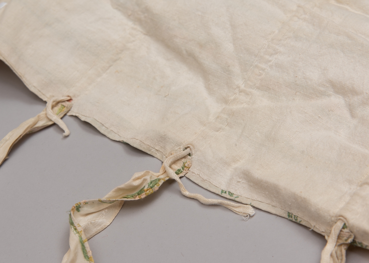 Dåpsløyert med pute samt løse ermer og en blondekrage. Løyerten er sydd av et ecrufarget silkestoff med stripemønster hvor det er innvevd blomster og blader. Løyerten lukkes med to sett knyteband, det ene settet er enkle bendelband som også snøres gjennom løpeganger, mens det andre er silkeband sydd av stoffet. Langs nederkant har løyerten en rynket kant av hovedstoffet samt et rynket dekorband av ensfarget, ecrufarget silke. Løyerten er fôret med linlerret. Ermene er sydd av hovedstoffet og har dekor av samme rynkede silkeband, men er uten fôr. Trolig har ermene vært tråklet til ei undertrøye som dåpsbarnet har hatt under reiven. Kragen, som er av tyllblonde, trolig i lin med silketråder og silkeband, er vid, så den har trolig vært rynket med ei snor og tråklet til undertrøya. Da barnet lå som en reivet bylt inne i løyerten, var det bare ermene som kom til syne, derfor var det ikke nødvendig med ei hel trøye. Alternativt kan det være at ermene tidligere har sittet på ei silketrøye som nå er fjernet.