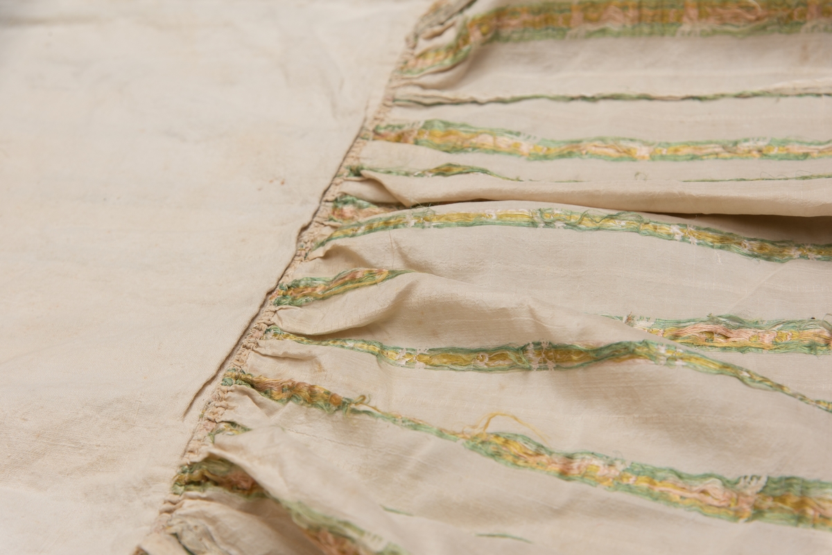 Dåpsløyert med pute samt løse ermer og en blondekrage. Løyerten er sydd av et ecrufarget silkestoff med stripemønster hvor det er innvevd blomster og blader. Løyerten lukkes med to sett knyteband, det ene settet er enkle bendelband som også snøres gjennom løpeganger, mens det andre er silkeband sydd av stoffet. Langs nederkant har løyerten en rynket kant av hovedstoffet samt et rynket dekorband av ensfarget, ecrufarget silke. Løyerten er fôret med linlerret. Ermene er sydd av hovedstoffet og har dekor av samme rynkede silkeband, men er uten fôr. Trolig har ermene vært tråklet til ei undertrøye som dåpsbarnet har hatt under reiven. Kragen, som er av tyllblonde, trolig i lin med silketråder og silkeband, er vid, så den har trolig vært rynket med ei snor og tråklet til undertrøya. Da barnet lå som en reivet bylt inne i løyerten, var det bare ermene som kom til syne, derfor var det ikke nødvendig med ei hel trøye. Alternativt kan det være at ermene tidligere har sittet på ei silketrøye som nå er fjernet.