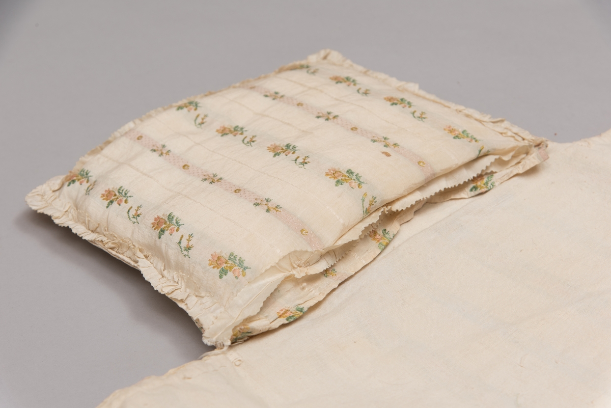 Dåpsløyert med pute samt løse ermer og en blondekrage. Løyerten er sydd av et ecrufarget silkestoff med stripemønster hvor det er innvevd blomster og blader. Løyerten lukkes med to sett knyteband, det ene settet er enkle bendelband som også snøres gjennom løpeganger, mens det andre er silkeband sydd av stoffet. Langs nederkant har løyerten en rynket kant av hovedstoffet samt et rynket dekorband av ensfarget, ecrufarget silke. Løyerten er fôret med linlerret. Ermene er sydd av hovedstoffet og har dekor av samme rynkede silkeband, men er uten fôr. Trolig har ermene vært tråklet til ei undertrøye som dåpsbarnet har hatt under reiven. Kragen, som er av tyllblonde, trolig i lin med silketråder og silkeband, er vid, så den har trolig vært rynket med ei snor og tråklet til undertrøya. Da barnet lå som en reivet bylt inne i løyerten, var det bare ermene som kom til syne, derfor var det ikke nødvendig med ei hel trøye. Alternativt kan det være at ermene tidligere har sittet på ei silketrøye som nå er fjernet.