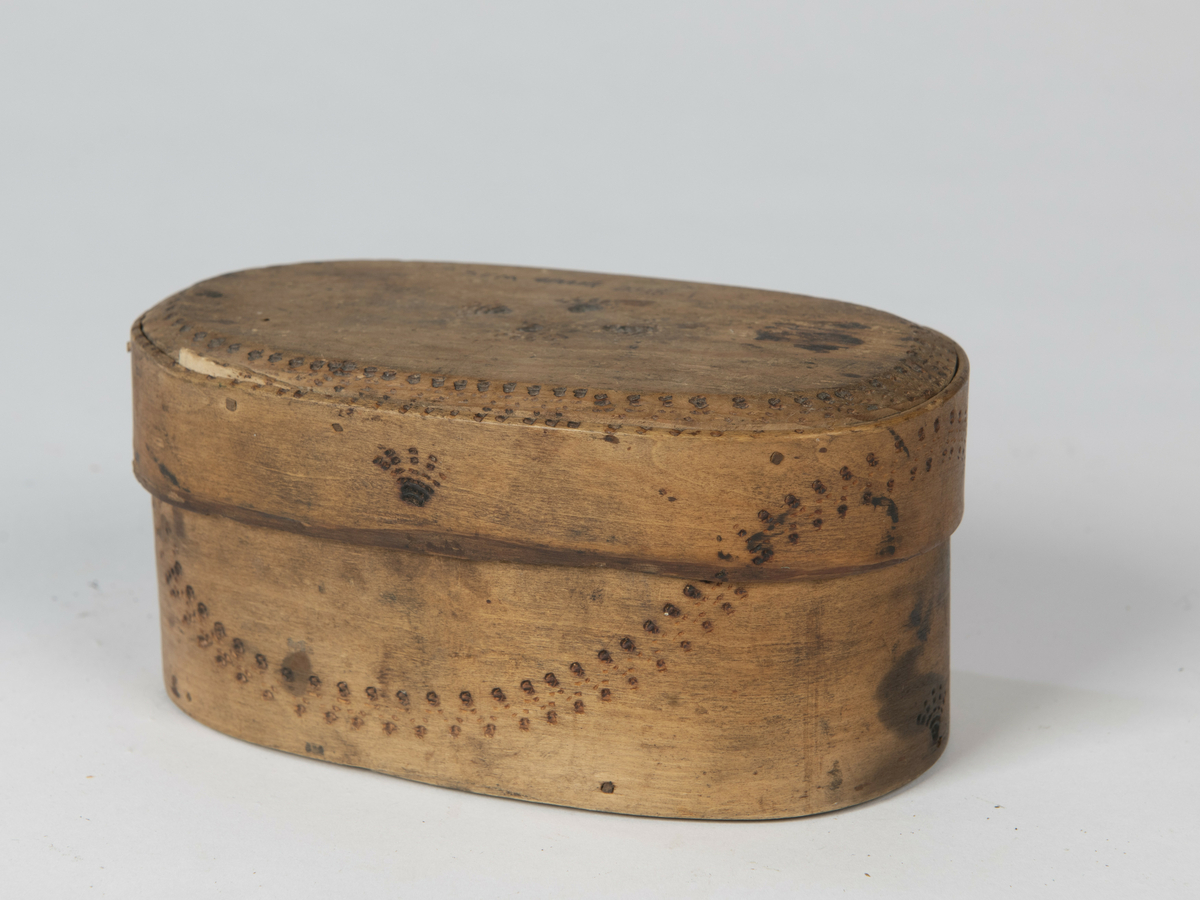Sveipet, oval ask med lokk. Utvendig svidekorert med sikksakkborder og andre motiver. Årstall 1704 og flere ulike merker under bunnen.