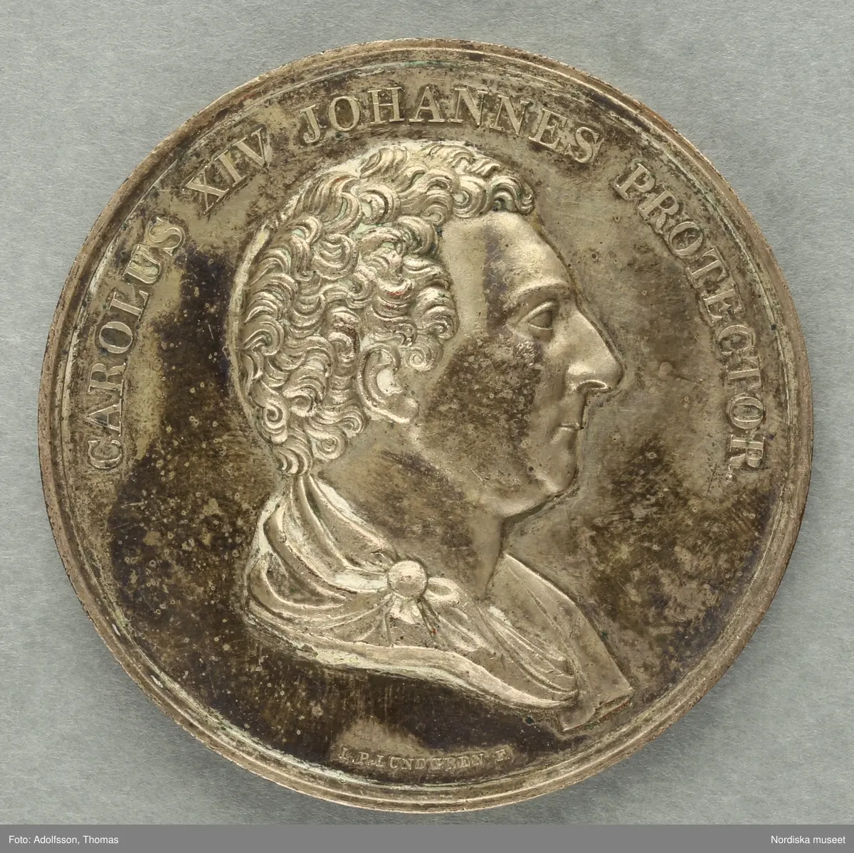 Huvudliggaren:
a-c
"3 minnespenningar. Öfver Karl XIV Johan.
a) I silfver. Jmfr Hildebrand, del II, sid 344, nr 34
b) I silfver. Jmfr H-d. del II, sid 345, nr 35.
c) I brons. Lika med b.