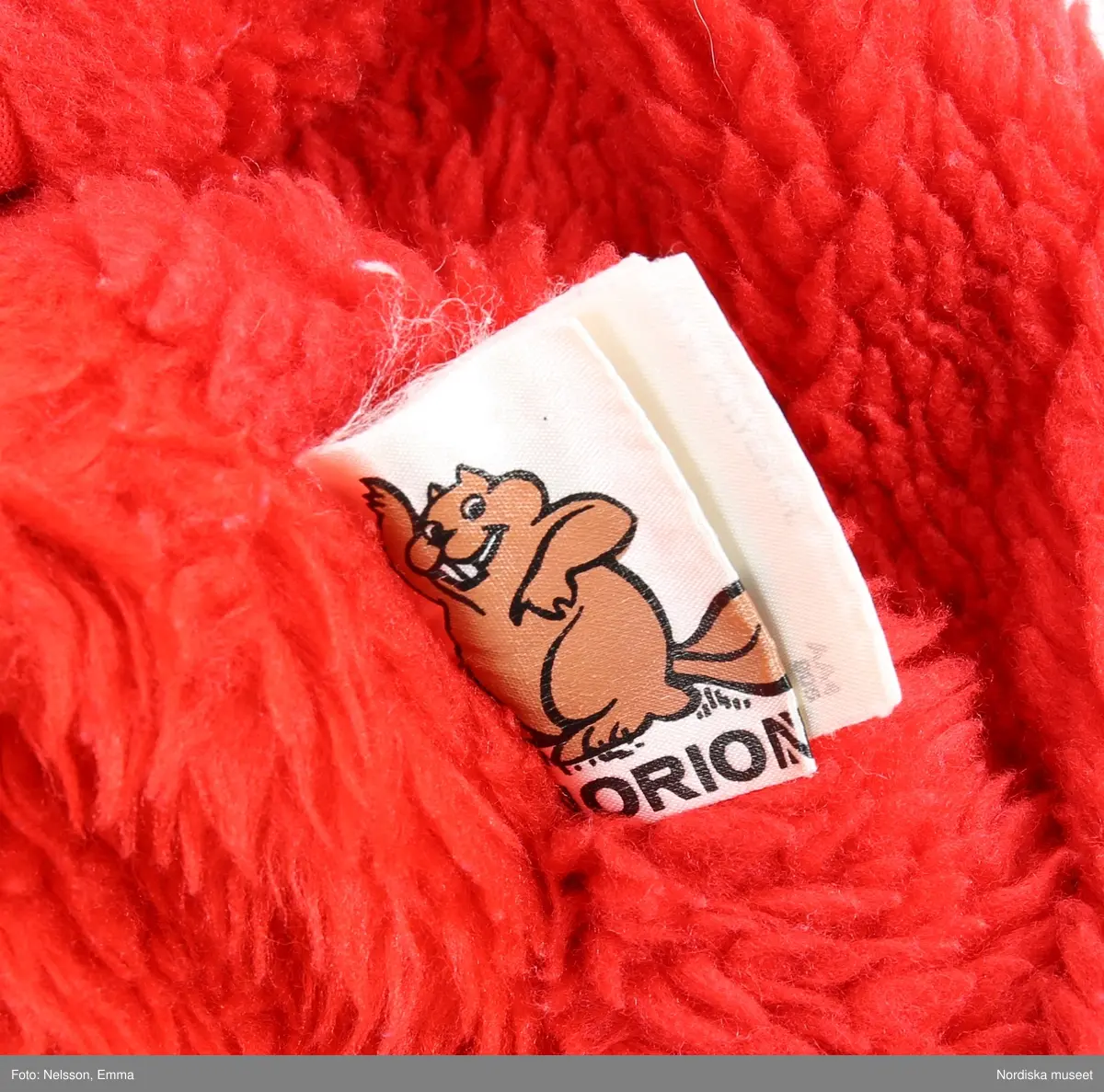 Katalogkort:
"Overall f. pojke av mörkblå s.k. "bäver-nylon" kypertvävnad av 50% polyamid och 50% bomull (mycket slitstark används till arbetskläder och barnkläder) fodrad med röd acrylpile i överdelen och med syntetvadd rutstickad med röd nylon i benen och ärmarna. 
Helskuren modell med besparing på axlarna fram, resår i midjan bak, isydd lång ärm med röda muddar av acryltrikå, lång rött blixtlås fram ned till grenen, rak krage med rött pilefoder, 2 påsydda framfickor med rött pilefoder och knäppta med slejf och nitad tryckknapp. Förstärkt med extra tyg på knäna. Fastsydd vitmetallhake på bröstet att fästa skidhandskarna i. Märke i vitt: Tuffis Reflexbricka i snöre fäst bak på kragen med säkerhetsnål."