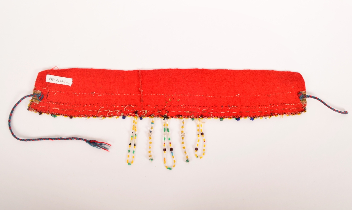 Lad, pannelin (a i raudt toskaftvove vadmel, påsett ein "perlebendel" av kvite, gule, grønne og svart perler. Perlesnor langst ytterste kanten av gule og blanke små perler, og med større grønne, blåe, brune og blanke perler med ca 2 cm mellomrom. Midt bak i nakken fem perleheng men blanke, gullblanke, blå, gule og svarte perler. 
Innanfor perlebendelen eit band i sølvagraman. 
Sekundert påsette ein kvit tyllblonde (b) (Ref. registreringar hjå BRF i 1978, 1981, 1988)
I kvar ende ei slindre snor