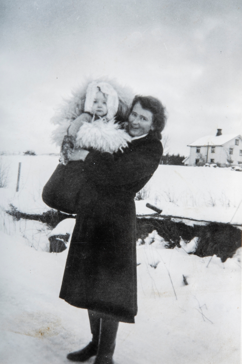 Karen Agnethe Flagstad (født Godager) med sønnen Arne Flagstad på armen. Bildet er tatt på Flagstad. I bakgrunnen ser vi hovedhuset på garden. Vinteren 1947.