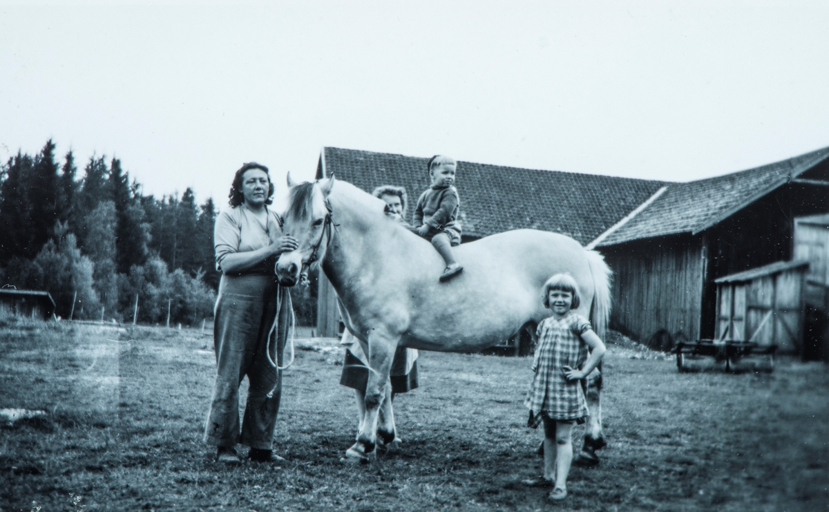 Bildet er tatt på Flagstad i 1947. Fra venstre Marie Alfarustad, Karen Agnethe, Arne Flagstad og Anne- Lise Nordli og hesten Blakken. I bakgrunnen ser vi låven og siloen til høyre og grisehuset til venstre. Høy til kuene ble båret fra låven og siloen, og over til steinfjøset. Marie var budeie og bodde i Drengestua. På Flagstad bodde det i denne perioden 9 kuer (Skjønne, Svartnok, Prinsesse, Hjerteros, Fredlin, Deilig, Berglin, Kveldsros, Blomstr), 200 høner, 4 griser og noen sauer.