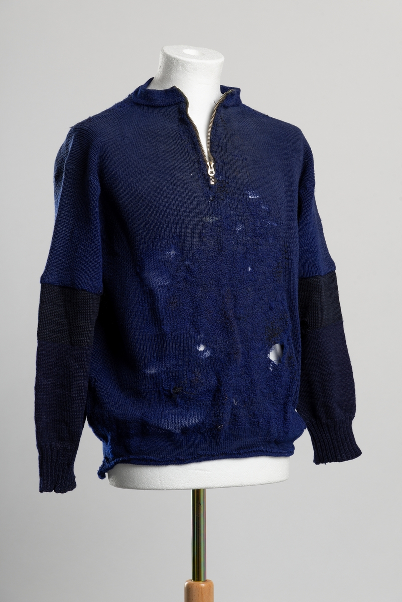 Ullgenser med glidelås i halsen. Genseren er stoppet på hele magen, langs hele midten av ryggen, ved albuene og langs vrangbordene. Ermene er byttet ut med nye fra albuen.