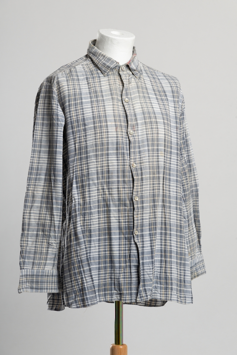 Grårutet herreskjorte med krage. Åpning i front med knappelukkning. Åtte plast knapper hvorav en er byttet ut med perlemorsknapp. Stoppet i ermesplittene. Stoppet og reparert i kragen. Diverse stoppede småhull på ermer og bakstykke.