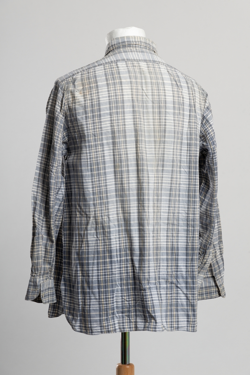 Grårutet herreskjorte med krage. Åpning i front med knappelukkning. Åtte plast knapper hvorav en er byttet ut med perlemorsknapp. Stoppet i ermesplittene. Stoppet og reparert i kragen. Diverse stoppede småhull på ermer og bakstykke.