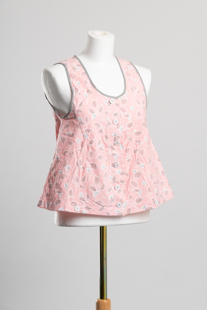 Hjemmesydd A-formet underliv av bomullsflanell med bladmønster. Ermehull og hals kantet med grått skråbånd. Åpning i front med knappelukkning, trukkede metallknapper.. To knapper langs falden i front.