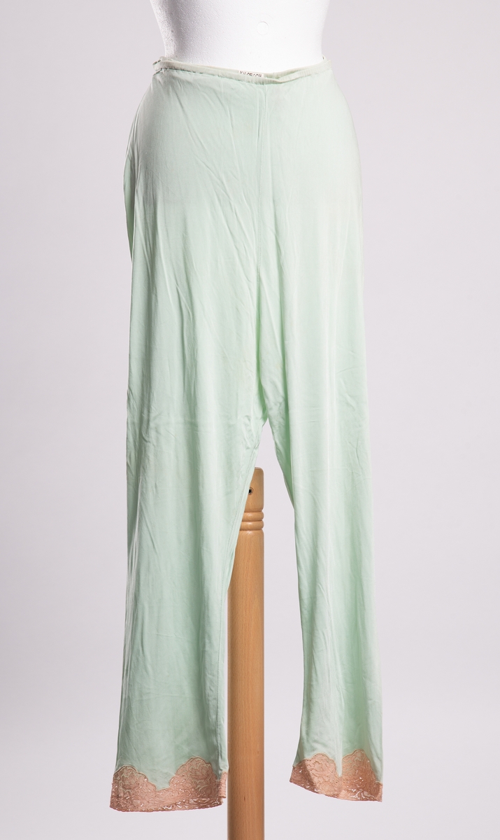 Mintgrønn pyjamasbukse til dame av strikket syntetfiber. Rette ben pyntet med blonder ved falden. Løpegang med strikk i livet.