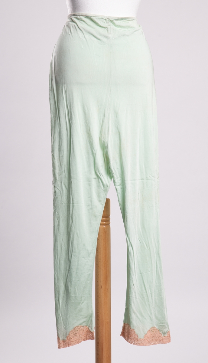 Mintgrønn pyjamasbukse til dame av strikket syntetfiber. Rette ben pyntet med blonder ved falden. Løpegang med strikk i livet.