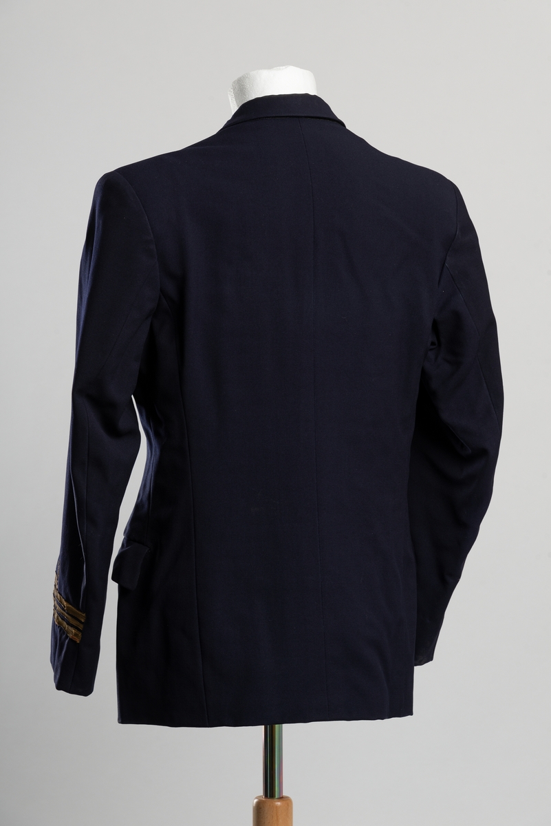 Losuniformsjakke av blått ulltekstil. Nederst på ermene tre gullbånd, to brede med et smalt i midten. Over båndene en krone i gull av metalltråd. Dobbeltsspent knappelukkning i front, gullfargede metallknapper med kronet anker som motiv. To lommer i front, pluss brystlomme. Innvendig lomme på høyreside. Foret med syntetstoff, hvit med sotre striper i ermer og svart i torso.