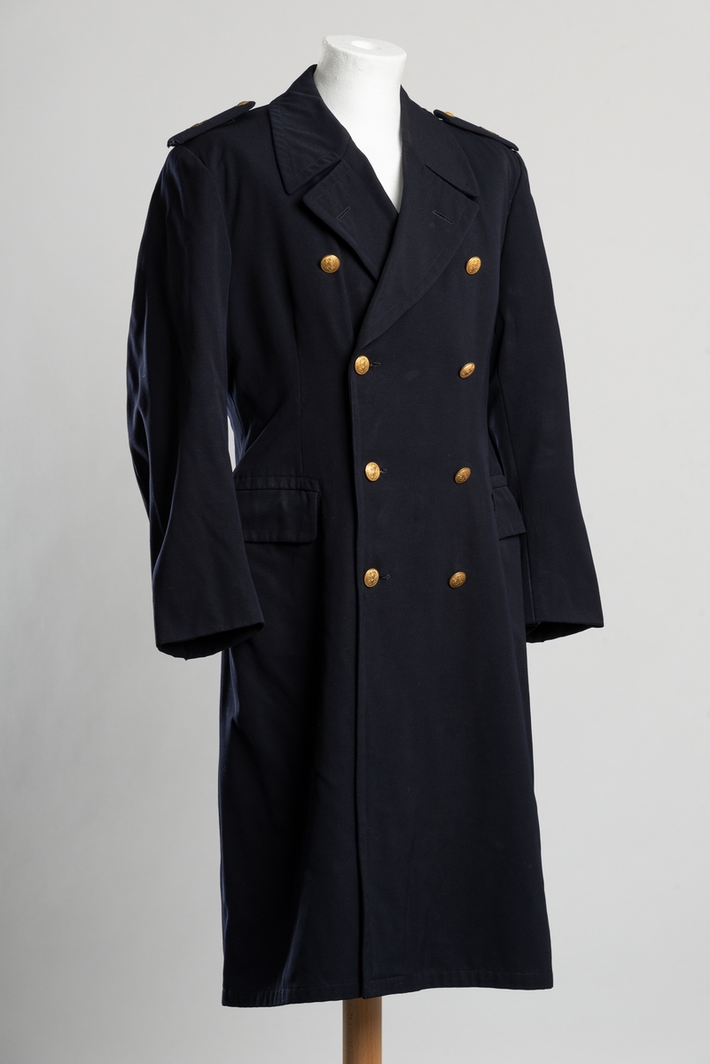 Uniformsfrakk av blått ullstoff. Dobbeltspent knappelukkning i front. Gullfargede metallknapper med Norges riksløve. To lommer i front, innerlomme på venstre side. Avtakbare epåletter med knapp og løvemblem. Pyntebånd med knappelukning i livet i ryggen. Splitt med knepping bak.