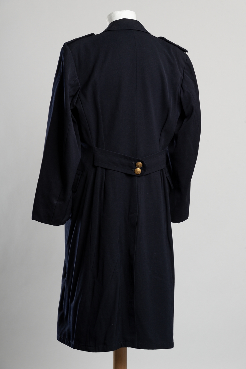 Uniformsfrakk av blått ullstoff. Dobbeltspent knappelukkning i front. Gullfargede metallknapper med Norges riksløve. To lommer i front, innerlomme på venstre side. Avtakbare epåletter med knapp og løvemblem. Pyntebånd med knappelukning i livet i ryggen. Splitt med knepping bak.