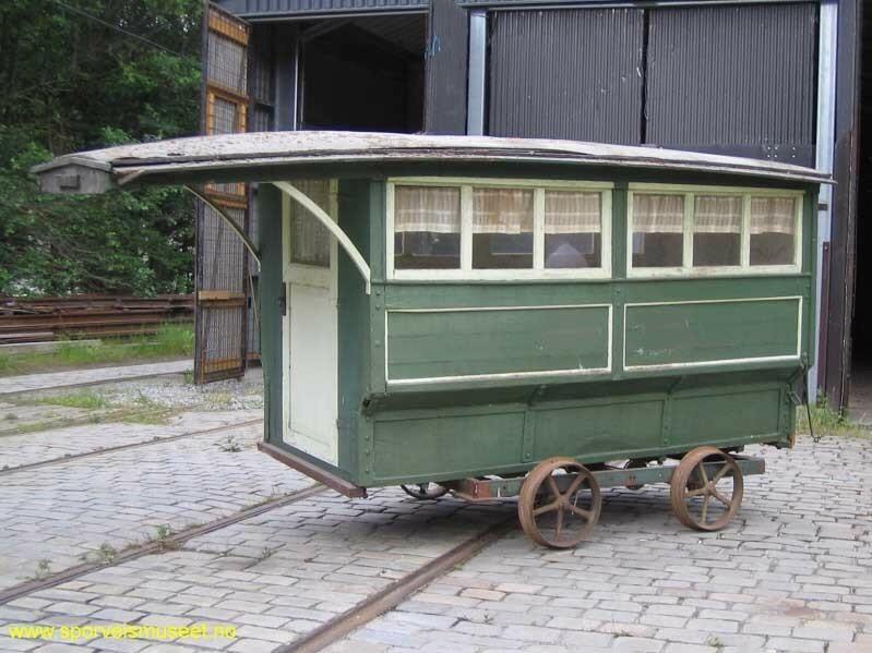 Buss i en grønn farge med hvit dør i front og hvite lister rundt vinduer. 