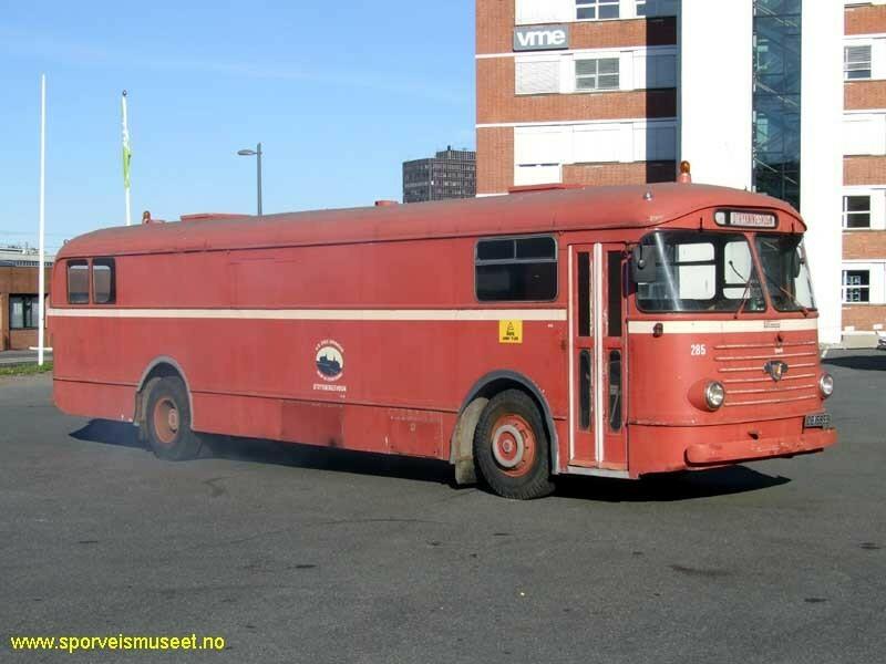 Rød buss med en kremhvit stripe som går rundt hele bussen. Bussen har inngangsdør i front ved sjåfør. På langsiden er det to vinduer, en ved inngangsdøren og en i bakre del. 