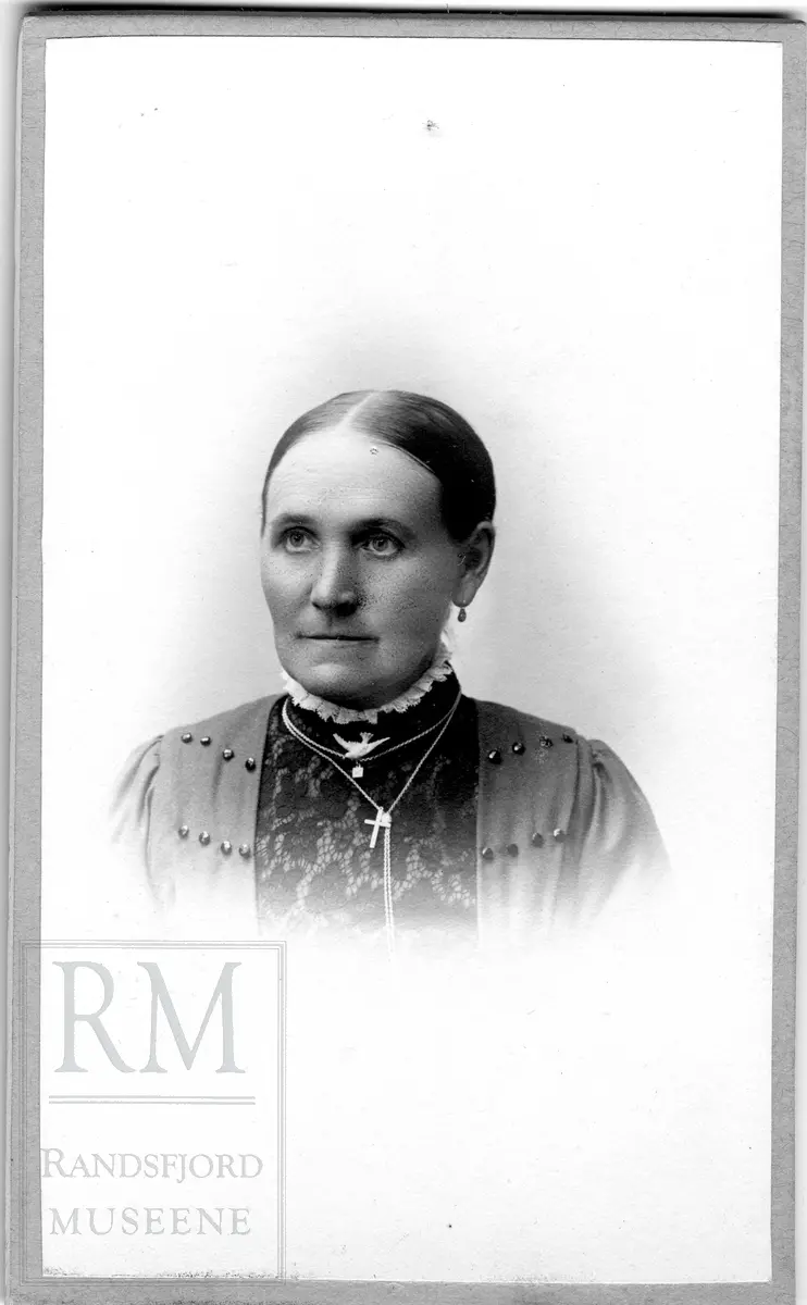 Brystbilde av eldre kvinne med kjeder med anheng (kors og fugl).