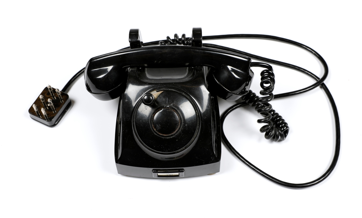 Svart telefonapparat i plast med sveiv, men uten tallskive.
Telefoner uten tallskive var tilknyttet manuelle telefonsentraler, og en brukte sveiva for å kommer i kontakt med sentralen, hvor det falt en klaff over linjejakken, et hvitt flagg og på større sentraler et lys over linjejakken. 
Denne het Elektrisk Burerau 1953 modell og ble produsert til 1967 i et antall 153 400 eksemplarer