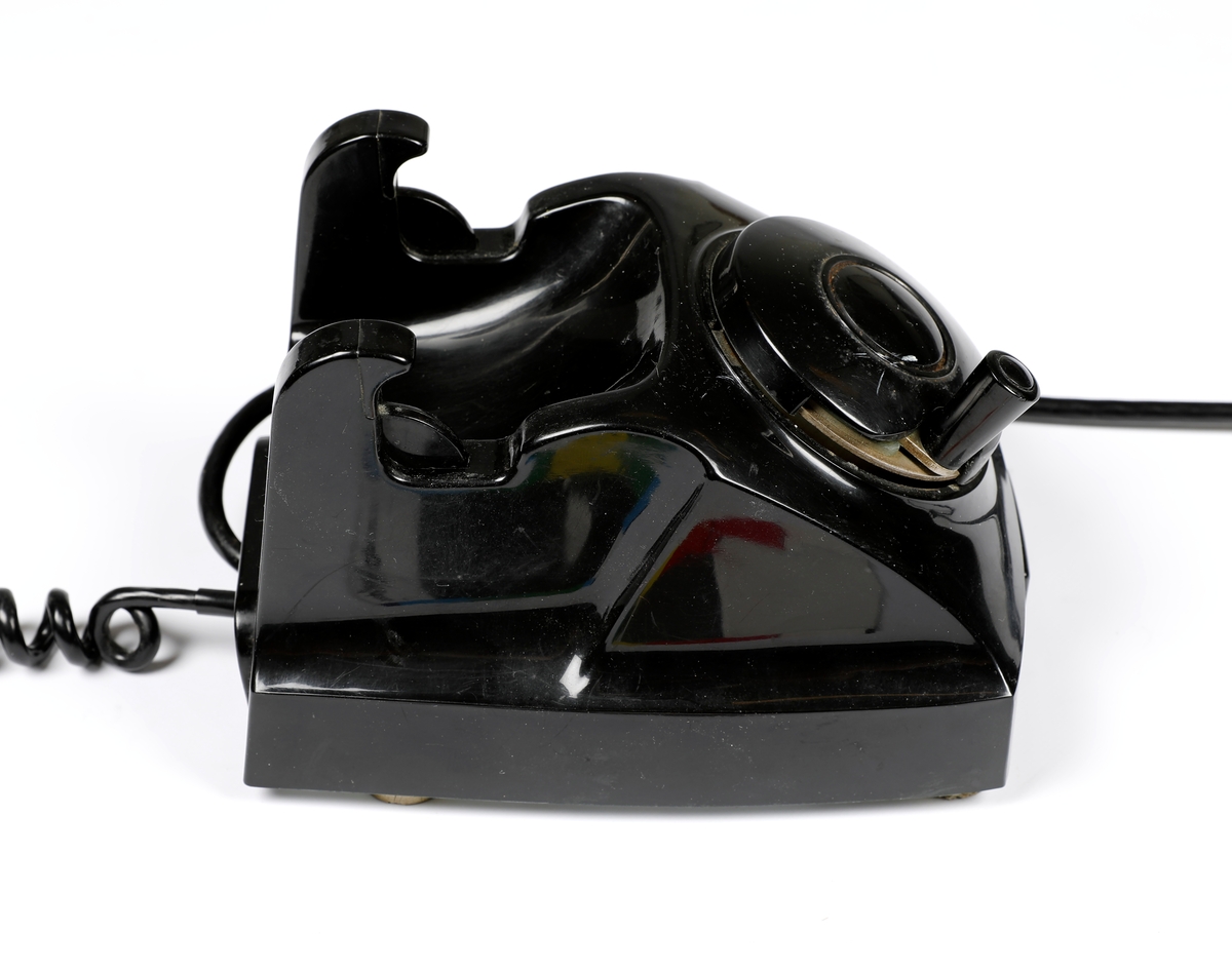 Svart telefonapparat i plast med sveiv, men uten tallskive.
Telefoner uten tallskive var tilknyttet manuelle telefonsentraler, og en brukte sveiva for å kommer i kontakt med sentralen, hvor det falt en klaff over linjejakken, et hvitt flagg og på større sentraler et lys over linjejakken. 
Denne het Elektrisk Burerau 1953 modell og ble produsert til 1967 i et antall 153 400 eksemplarer