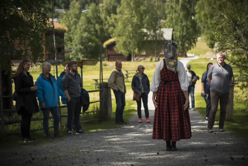 Dame i bunad som holder omvising for ei gruppe