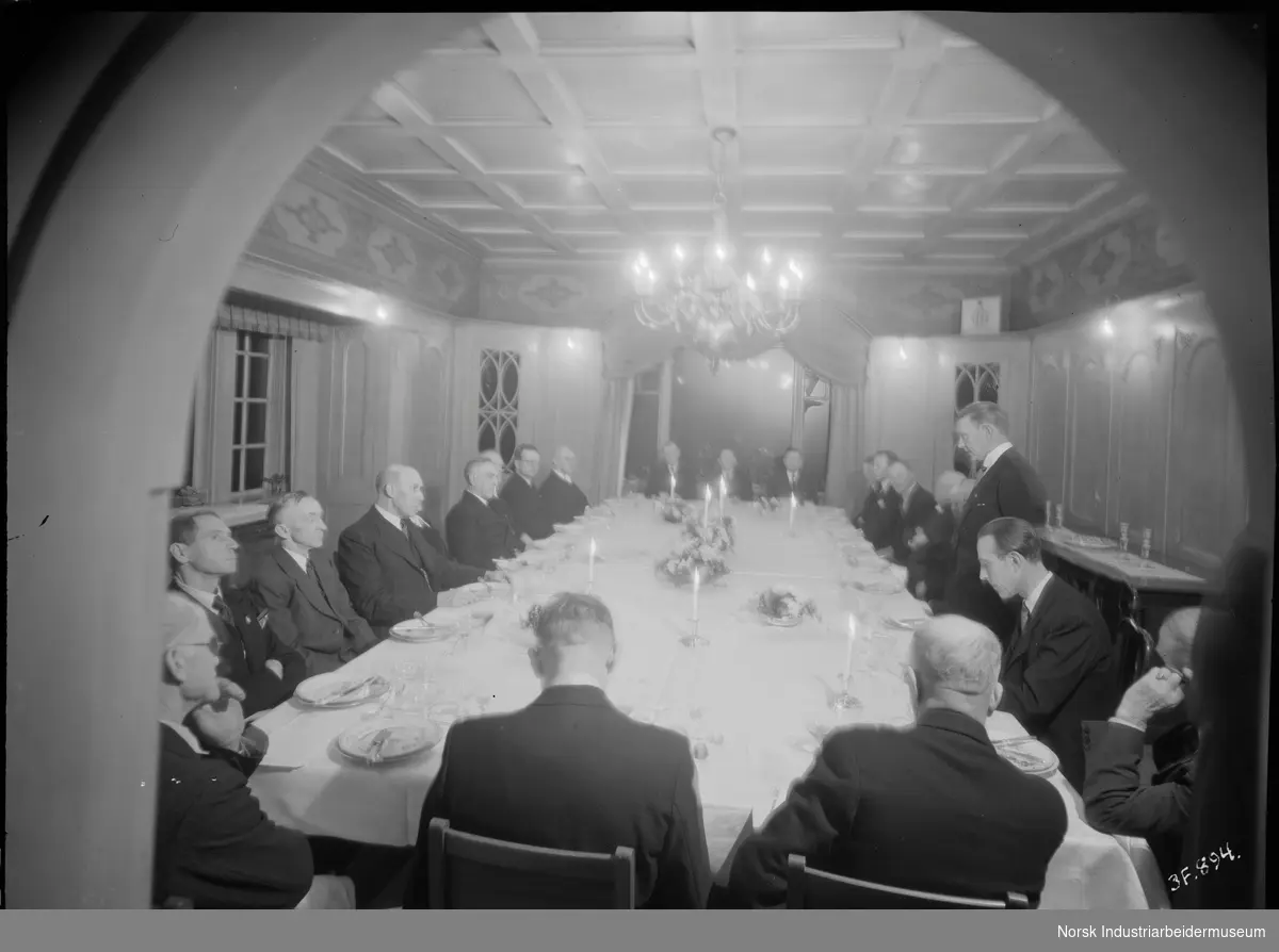 40 og 25 års. jubilanter 1945. Mennesker sittende rundt dekket bord. Mann stående ved bordet, holder muligens tale.