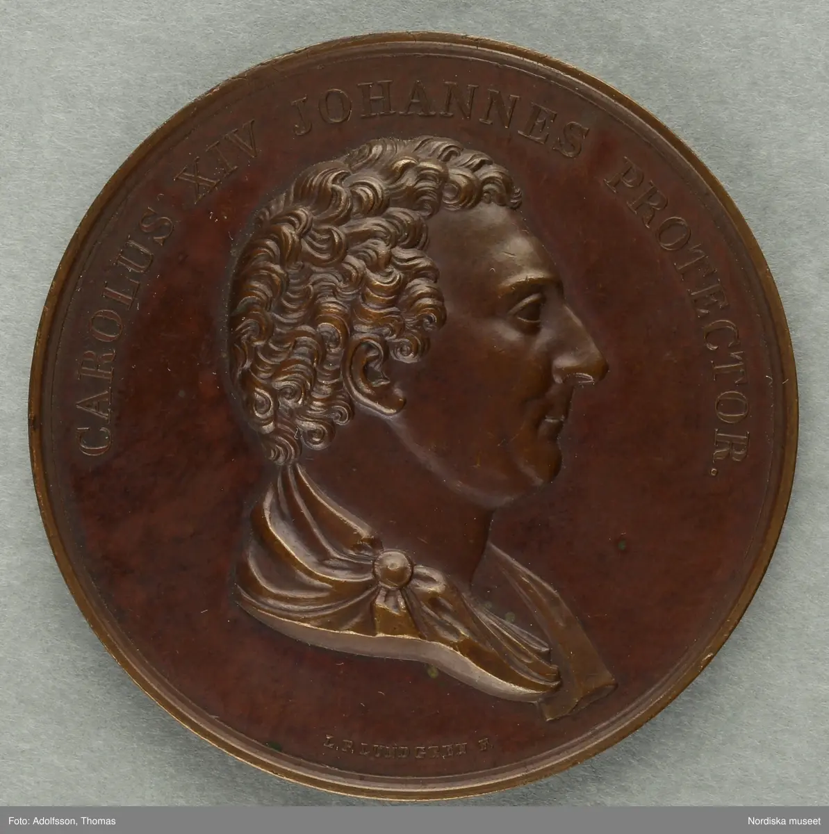 Huvudliggaren:
a-c
"3 minnespenningar. Öfver Karl XIV Johan.
a) I silfver. Jmfr Hildebrand, del II, sid 344, nr 34
b) I silfver. Jmfr H-d. del II, sid 345, nr 35.
c) I brons. Lika med b.